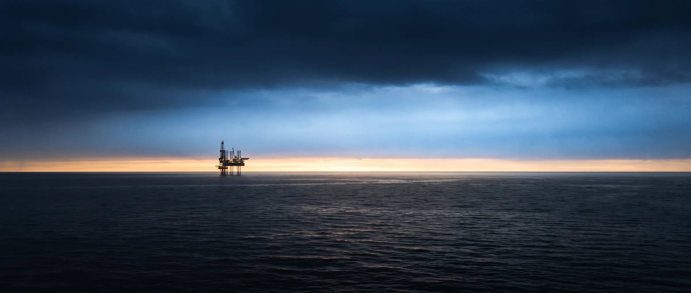 O mar aberto no primeiro clarão do dia, com uma plataforma offshore ainda iluminada ao longe