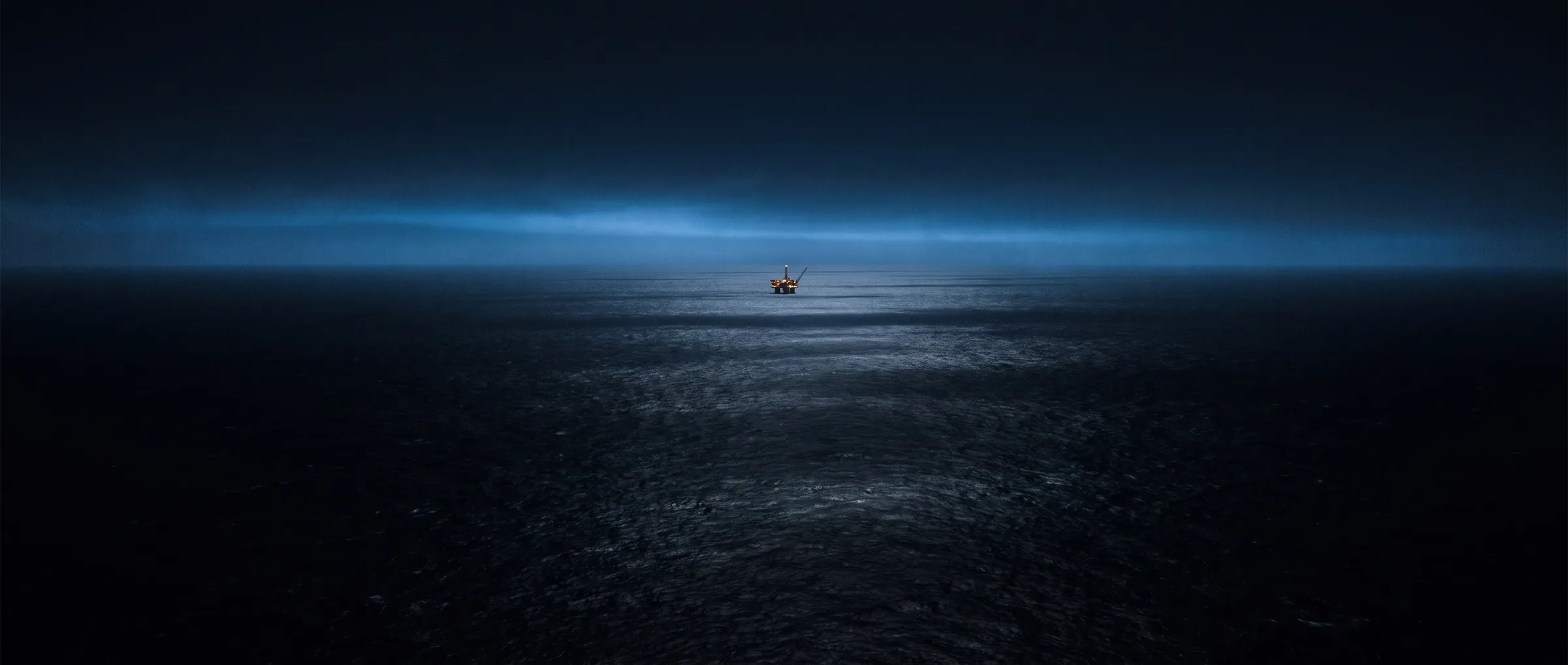 Mar aberto à noite, com uma plataforma offshore distante no horizonte